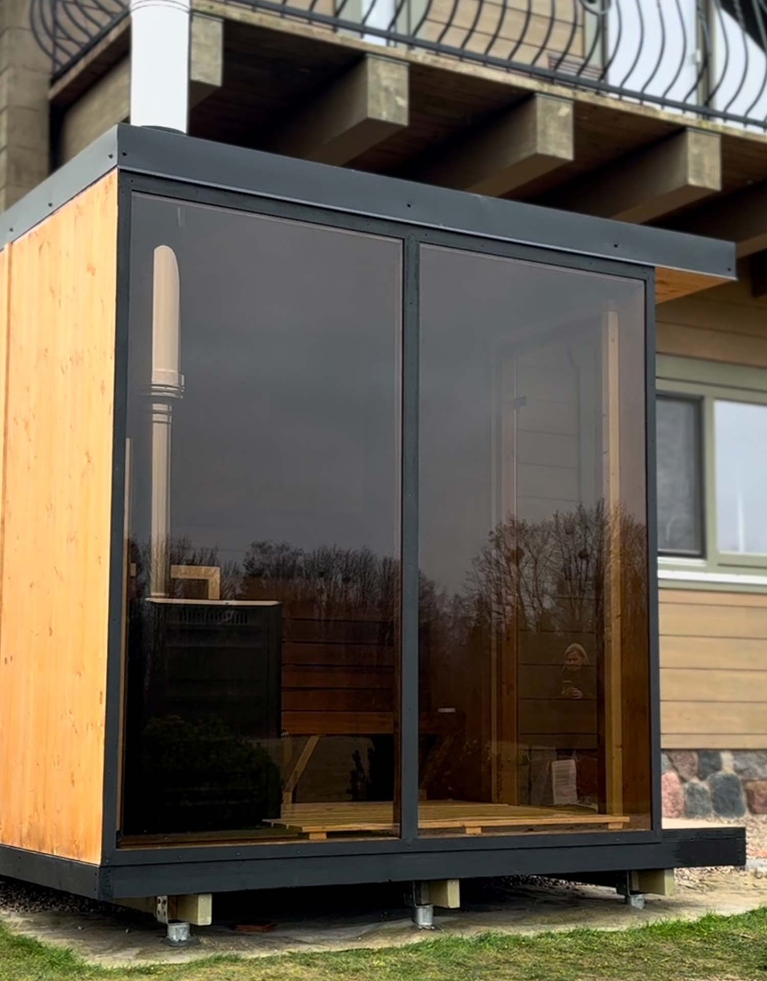 Modulsauna mit getönter Panorama-Glasfront und Lärchenholz neben einem Wohnhaus