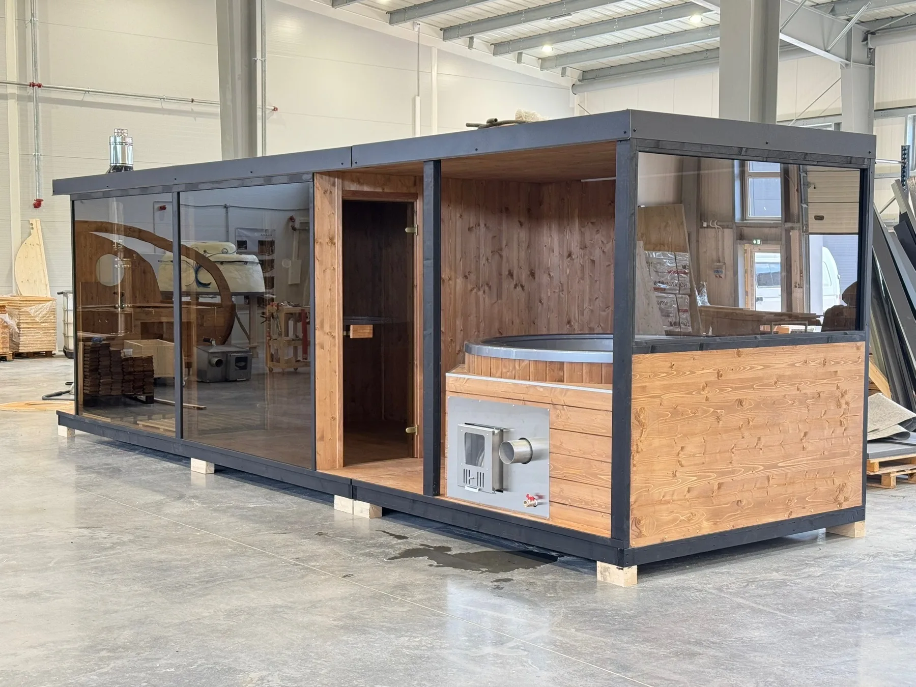 Schwarze Modulsauna mit Glasfront und integriertem Hot Tub in der Fertigungshalle