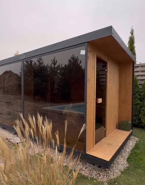 Längliche Gartensauna mit dunkler Glasfront und Holzeingang am Pool